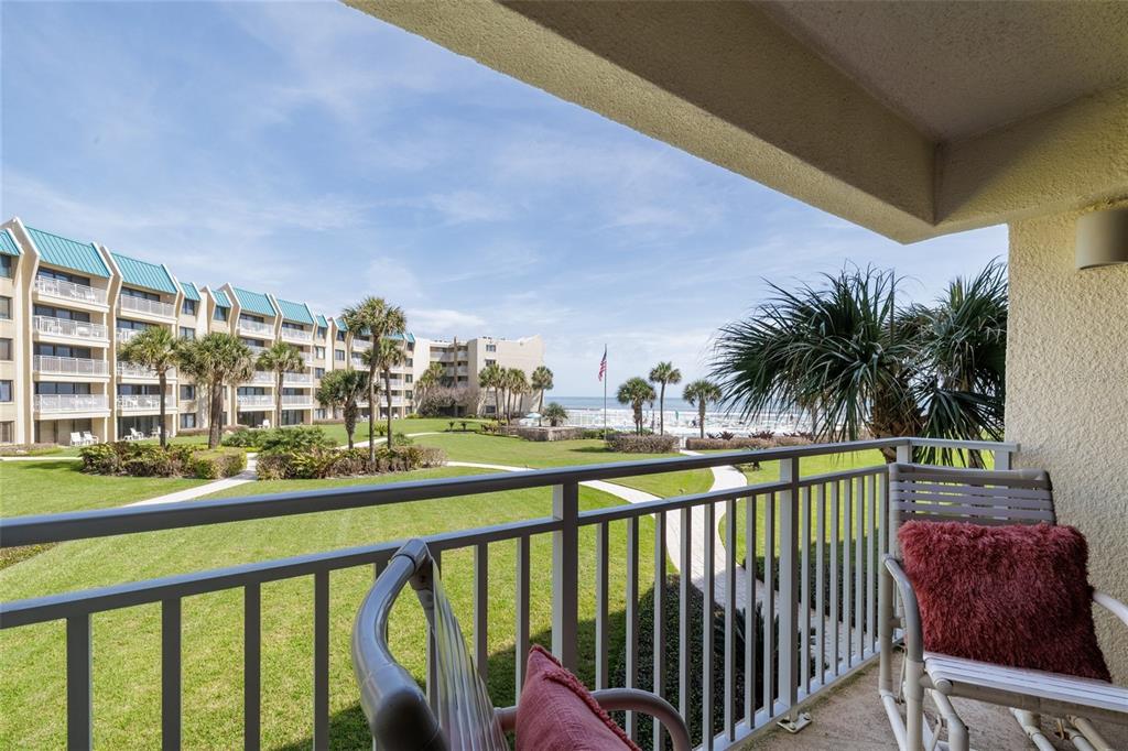 A balcony overlooks a grassy courtyard, palm trees, and the ocean in the distance — 4501 S ATLANTIC AVENUE UNIT 209, NEW SMYRNA BEACH, FL