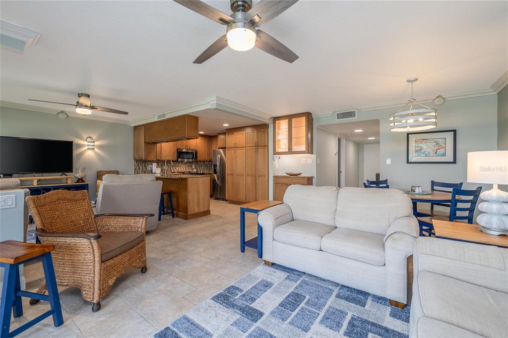 An open-concept living room and kitchen featuring tile floors, wood cabinetry, and neutral furniture — 4501 S ATLANTIC AVENUE UNIT 209, NEW SMYRNA BEACH, FL