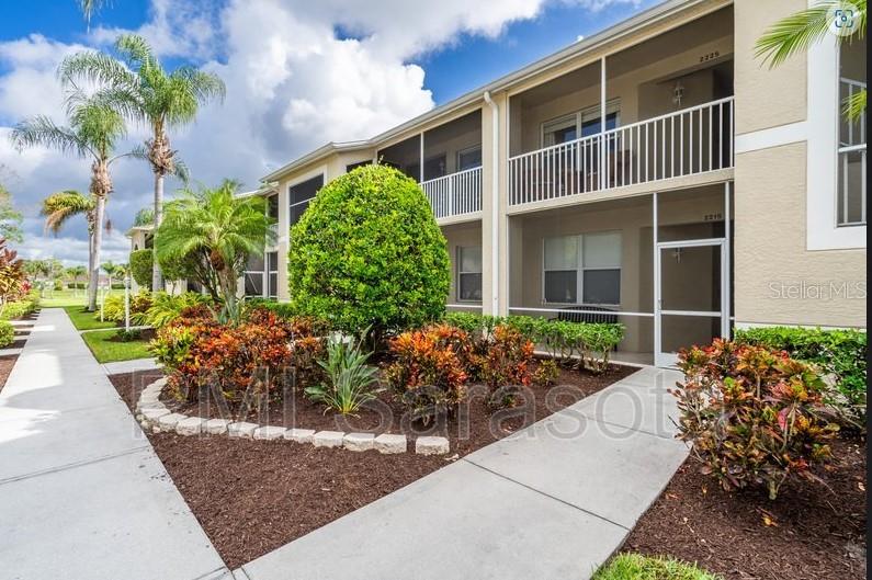 A two-story apartment building features screened-in balconies and landscaped garden beds with palm trees — 5320 HYLAND HILLS AVENUE UNIT 2225, SARASOTA, FL