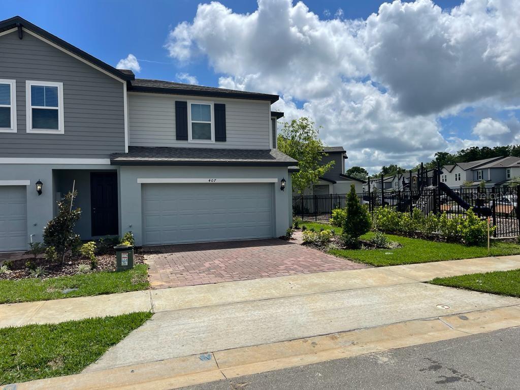 A two-story gray townhouse with a paved driveway and a garage at street level — 407 LEGACY LOOP, DAVENPORT, FL