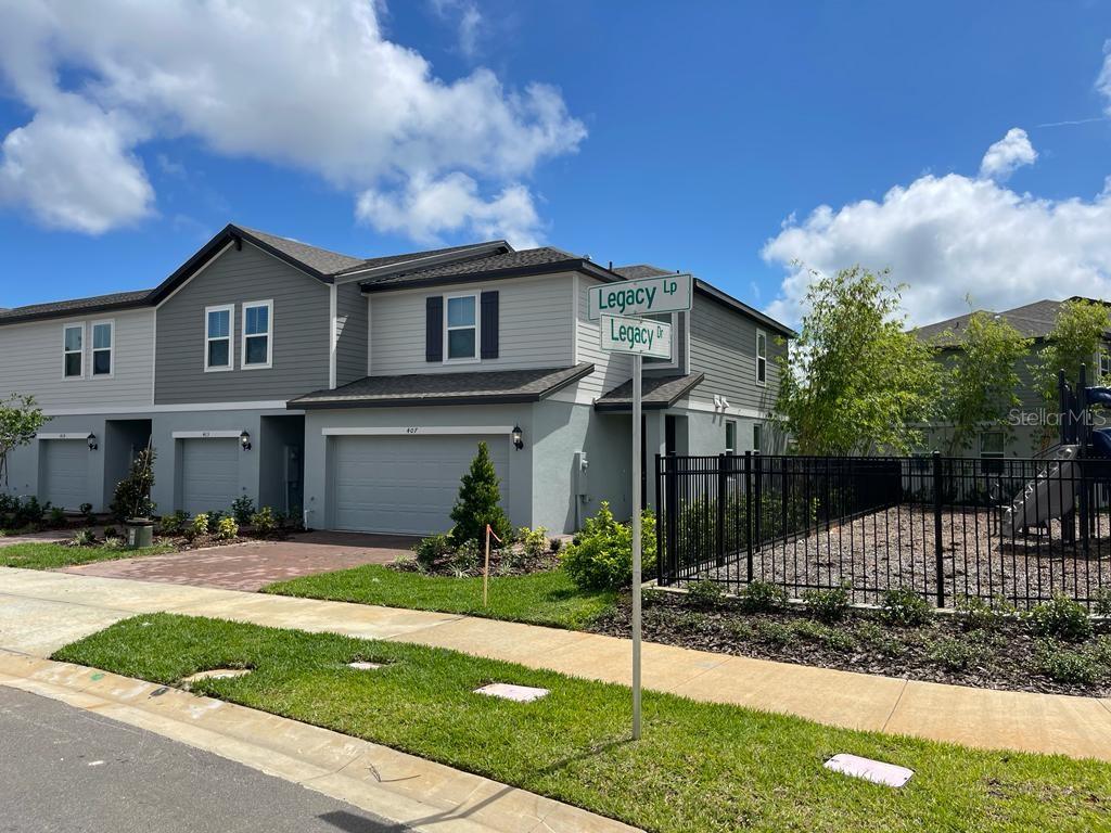 A two-story townhouse with a gray exterior and a street sign in the foreground — 407 LEGACY LOOP, DAVENPORT, FL