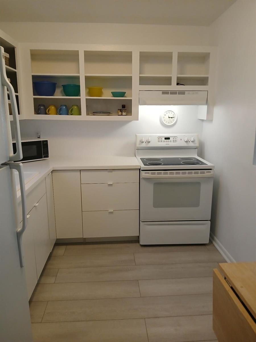 A white kitchen features open shelving, a white electric stove, and light-colored wood-look flooring — 721 Lori Drive # 309, Palm Springs FL 33461, PALM SPRINGS, FL