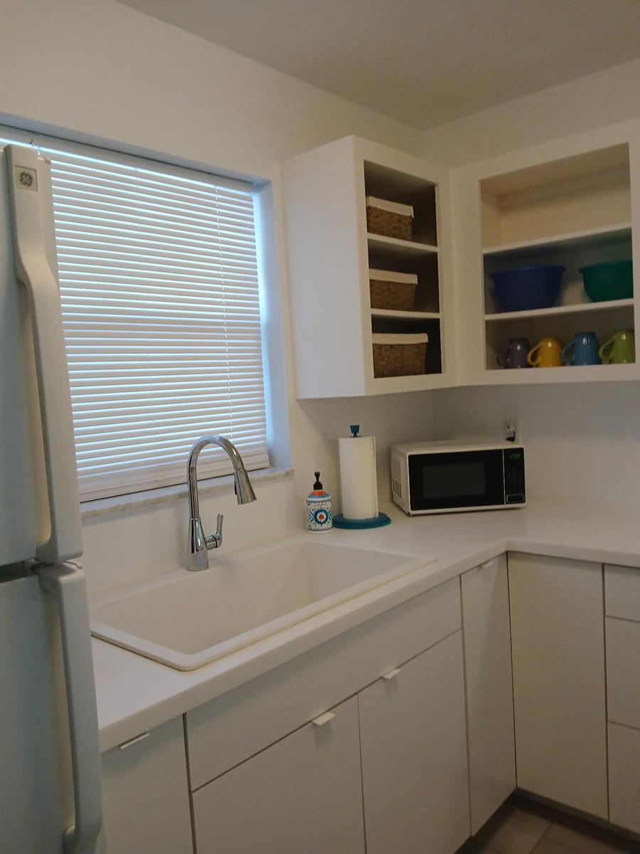 A white kitchen features a sink, microwave, open shelving, and white cabinets — 721 Lori Drive # 309, Palm Springs FL 33461, PALM SPRINGS, FL