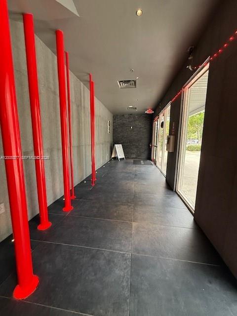 A covered walkway features bright red support columns, dark tiled flooring, and glass-paneled doors — University Dr, Coral Springs FL 33071, CORAL SPRINGS, FL