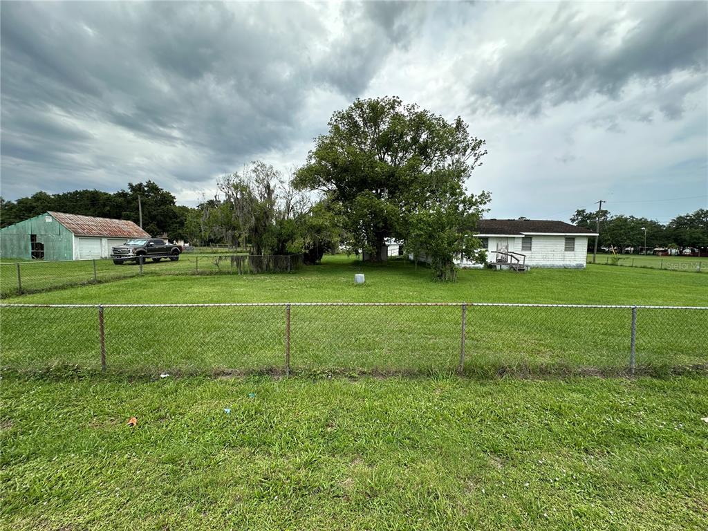 A grassy yard features a chain-link fence, a white house, and a green metal shed — 1886 PLEASANT HILL ROAD, KISSIMMEE, FL