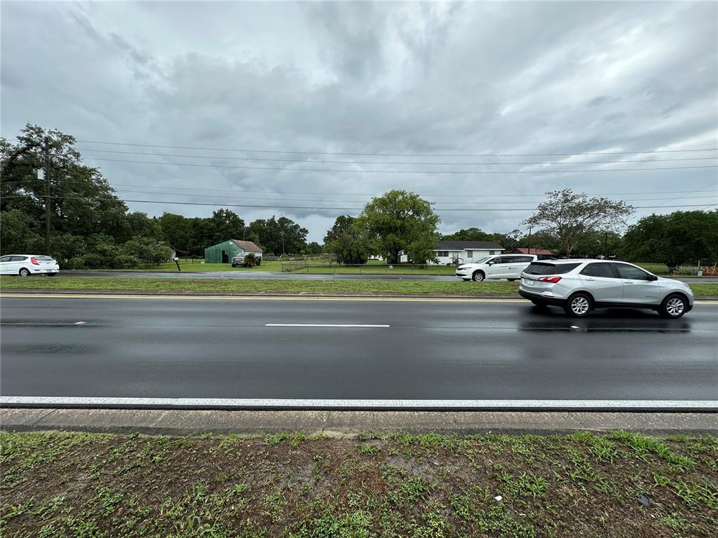 A view of a wet road with passing cars and a grassy lot beyond — 1886 PLEASANT HILL ROAD, KISSIMMEE, FL
