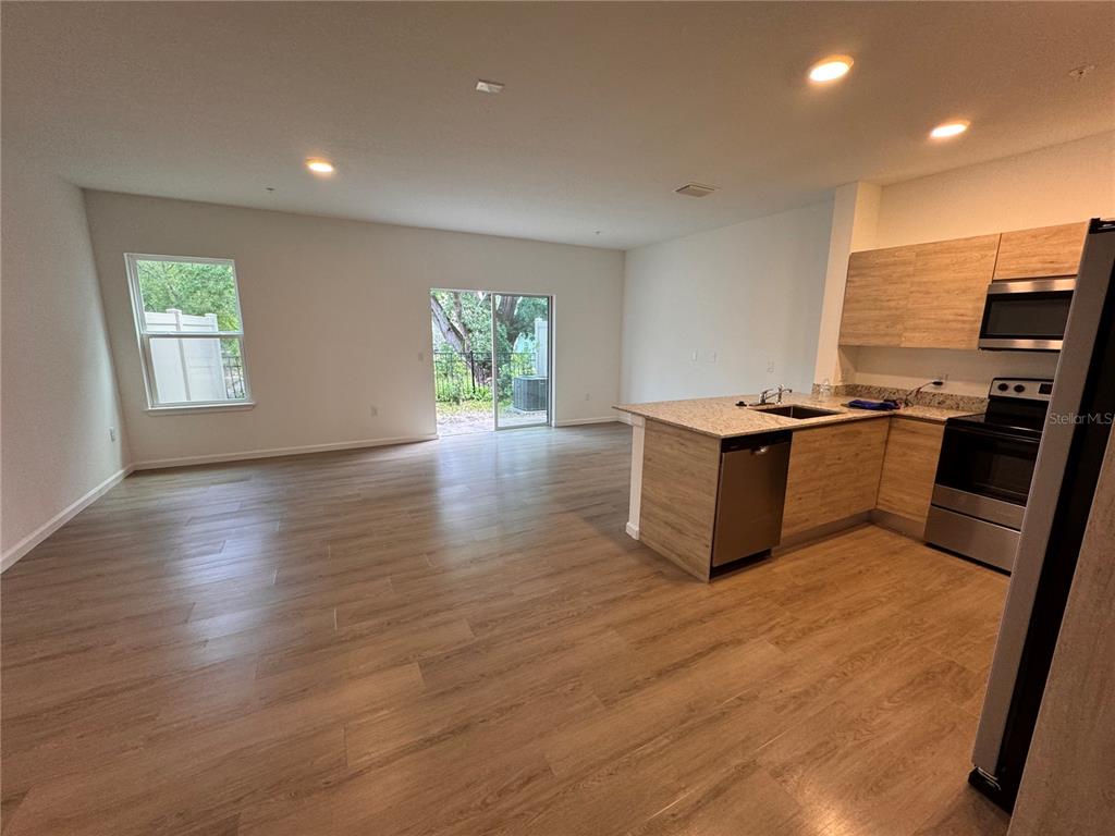 An open-concept living area features wood-look flooring, a kitchen with light wood cabinets, and sliding doors — 1209 SOUTHSTATION PLACE UNIT 306, ORLANDO, FL