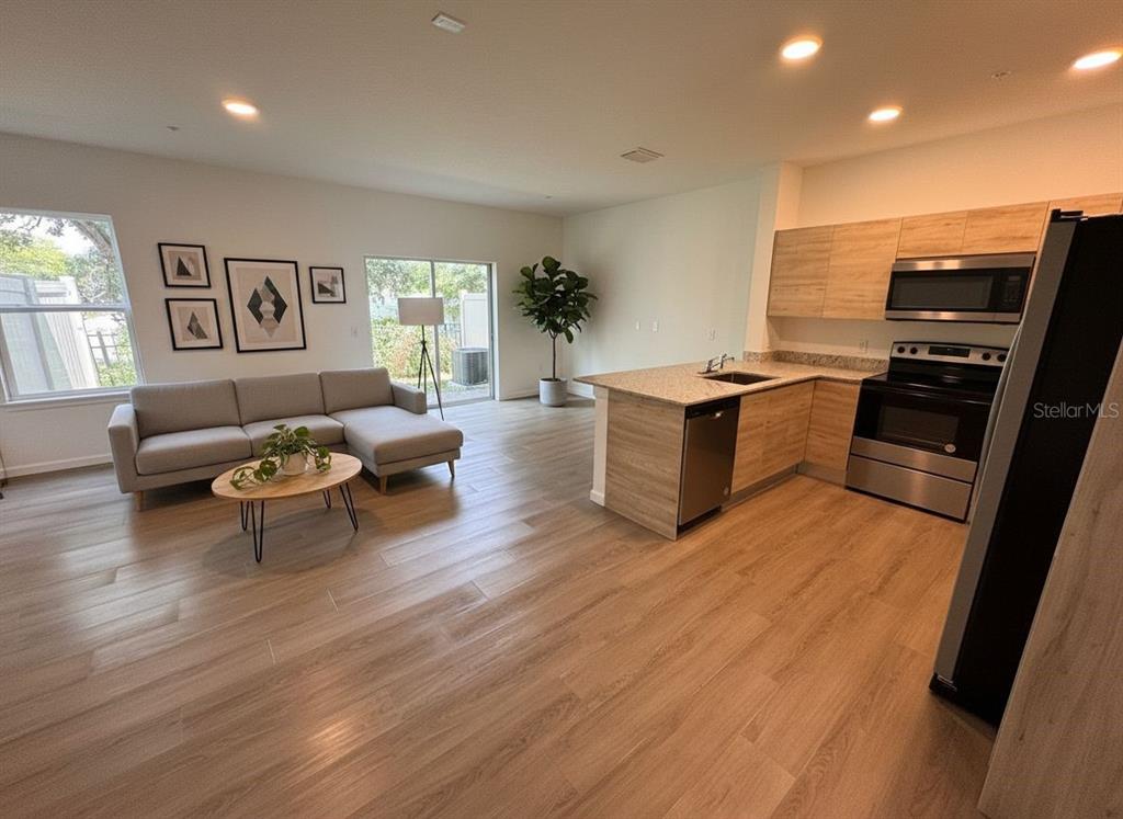 An open-concept living room and kitchen with light wood flooring and stainless steel appliances — 1209 SOUTHSTATION PLACE UNIT 306, ORLANDO, FL