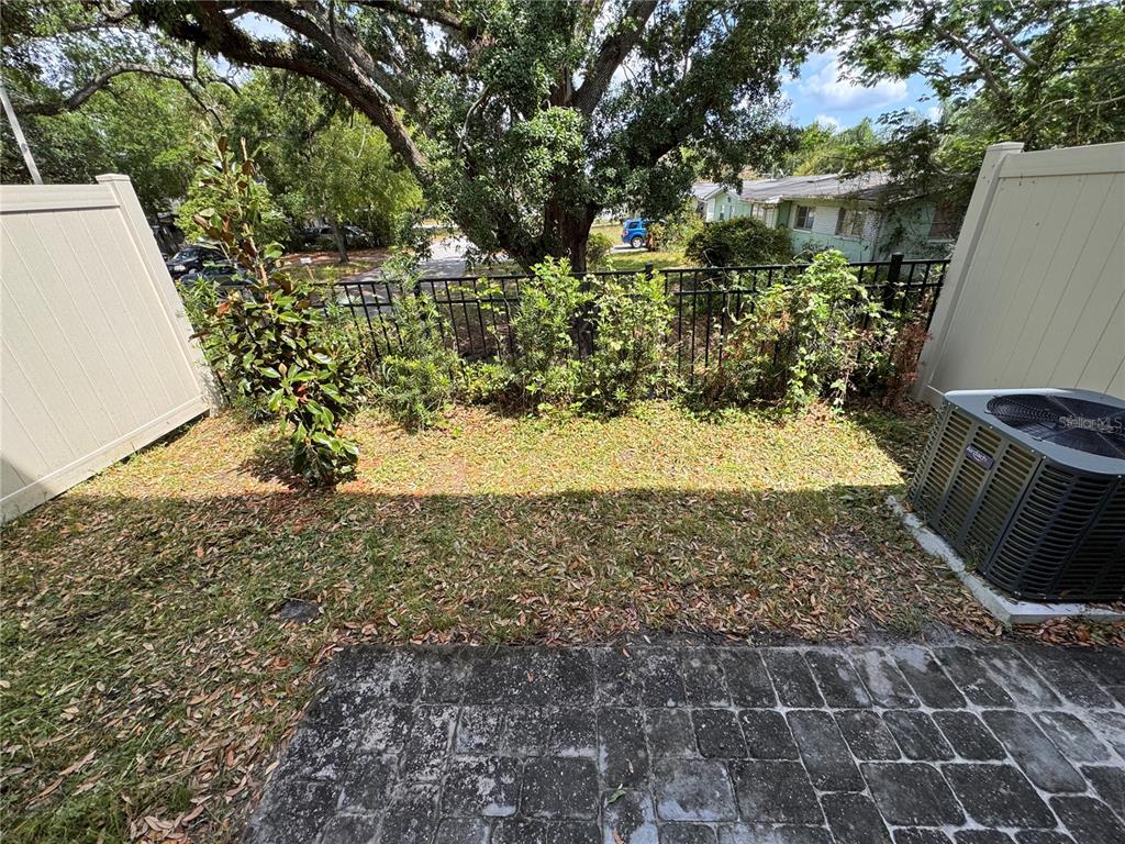 A small backyard patio with a paved area, grass, landscaping, and an air conditioning unit — 1209 SOUTHSTATION PLACE UNIT 306, ORLANDO, FL