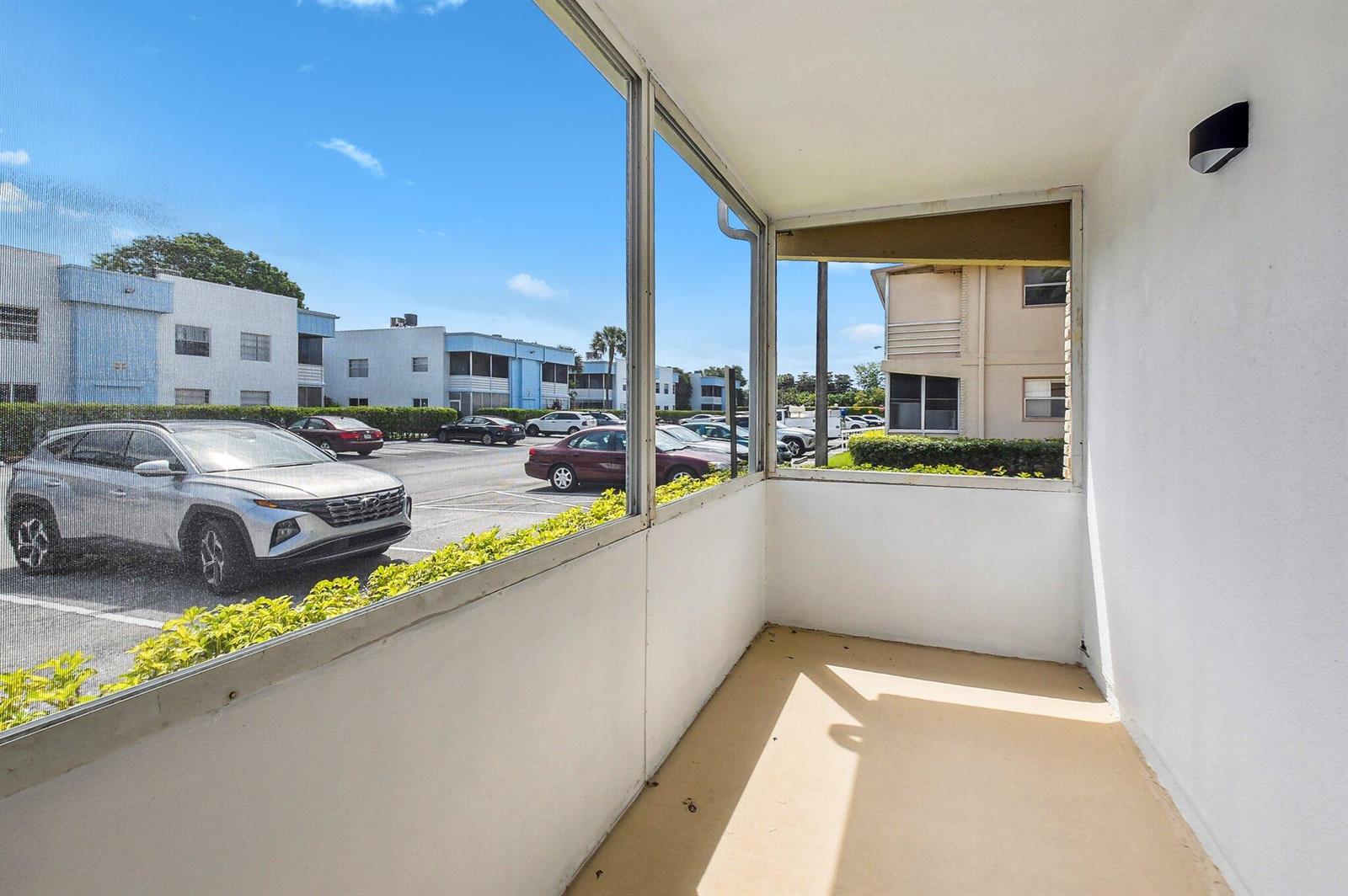 A screened-in porch with a beige floor overlooks a parking lot and apartment buildings — 447 Saxony J Way # J, Delray Beach FL 33446, DELRAY BEACH, FL