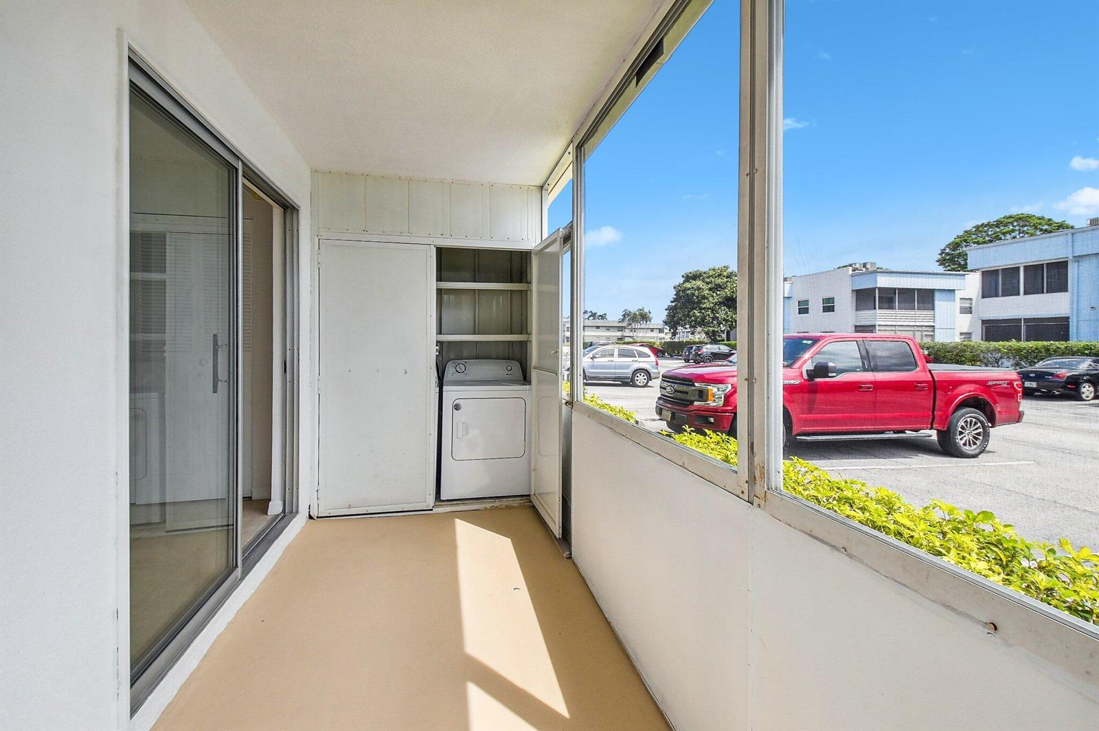 A screened-in porch features a laundry closet with a dryer and a view of parking — 447 Saxony J Way # J, Delray Beach FL 33446, DELRAY BEACH, FL