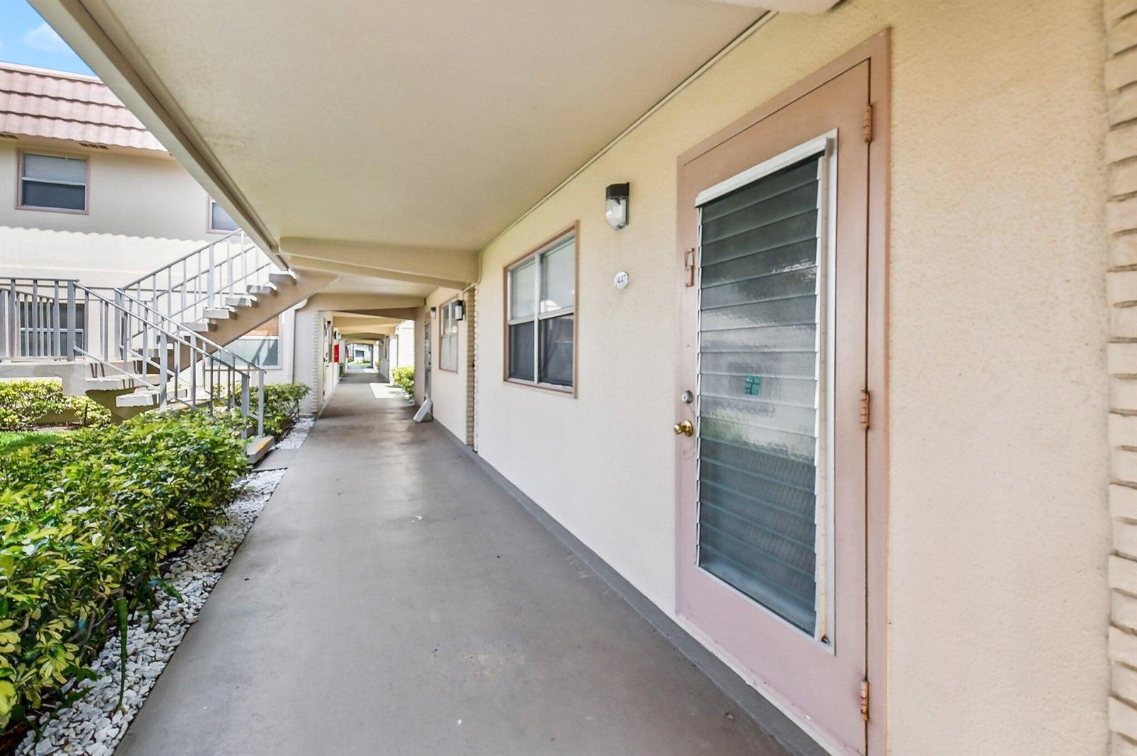An exterior walkway leads past apartment doors and a staircase in a residential complex — 447 Saxony J Way # J, Delray Beach FL 33446, DELRAY BEACH, FL