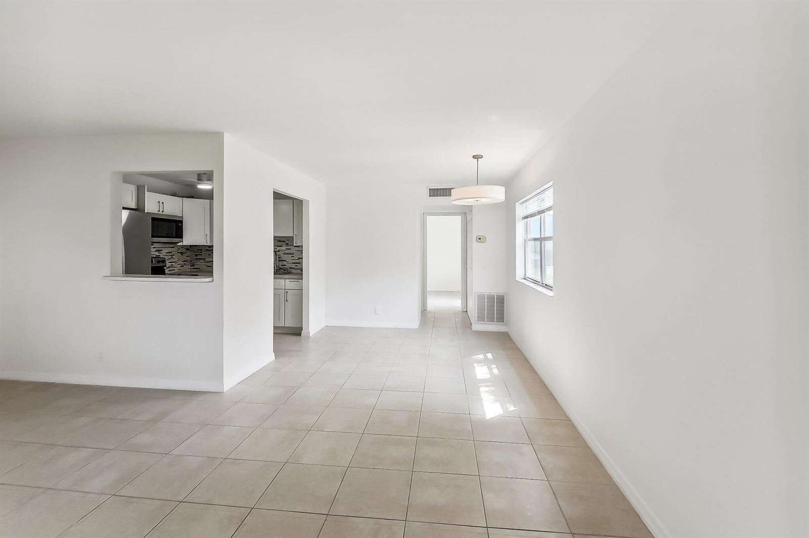 An open-concept dining area features white walls, beige tile flooring, and a pass-through kitchen window — 447 Saxony J Way # J, Delray Beach FL 33446, DELRAY BEACH, FL