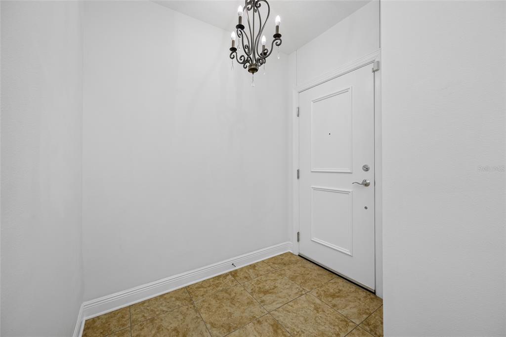 An entryway features a white door, tiled flooring, and a decorative chandelier — 628 CLEVELAND STREET UNIT 1313, CLEARWATER, FL