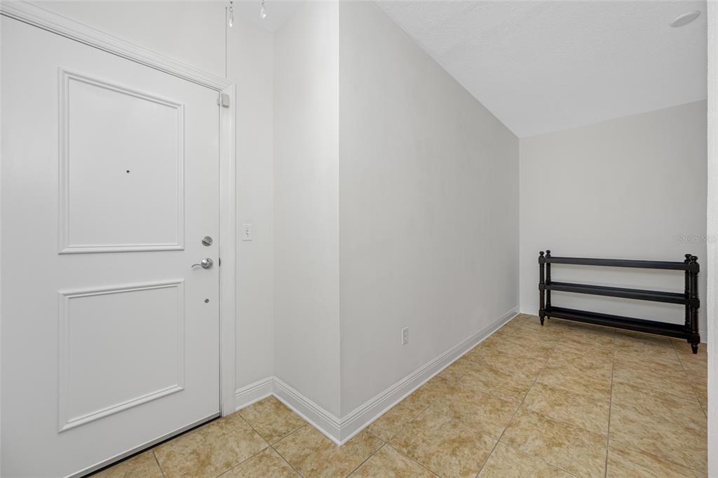 An entryway with a white door, light-colored tile flooring, and a black metal shoe rack — 628 CLEVELAND STREET UNIT 1313, CLEARWATER, FL