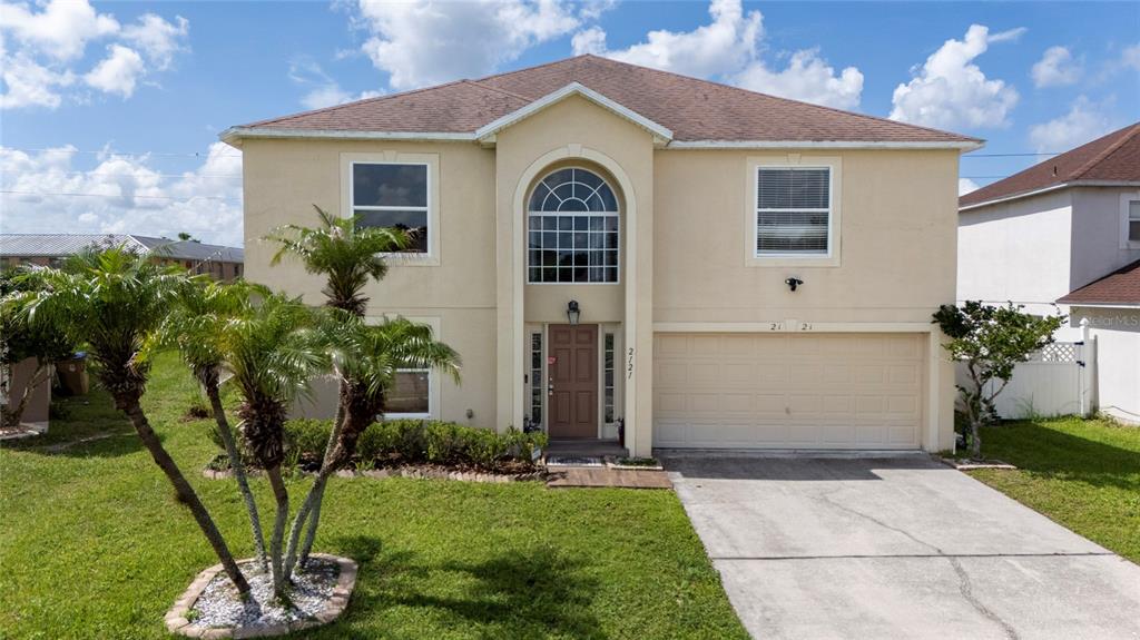 A two-story beige house with a tan shingle roof, arched window, and a concrete driveway — 2121 BLACKSTONE LANDING DRIVE, KISSIMMEE, FL