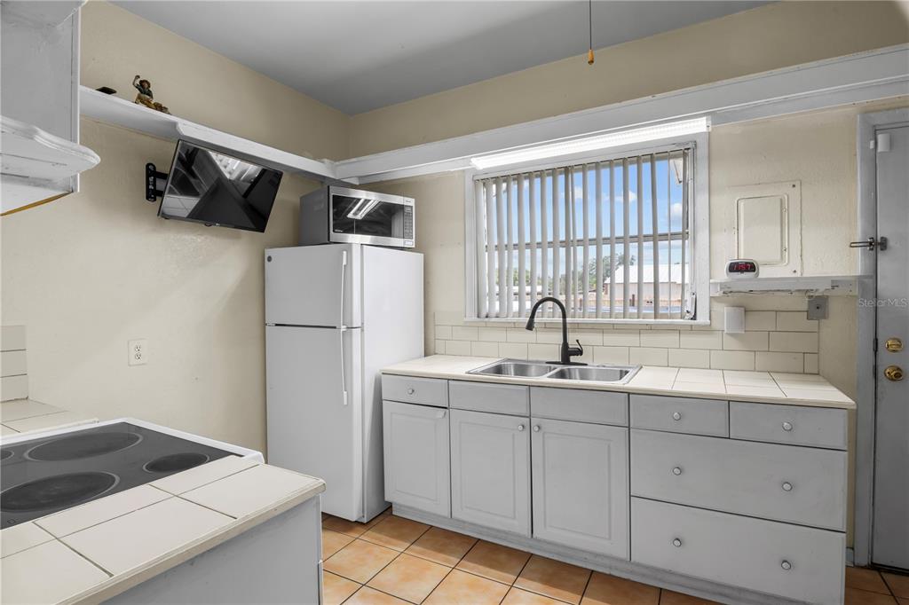 A kitchen features white cabinets, a tiled countertop, a stainless steel sink, and a refrigerator — 4517 KENILWORTH BOULEVARD, SEBRING, FL