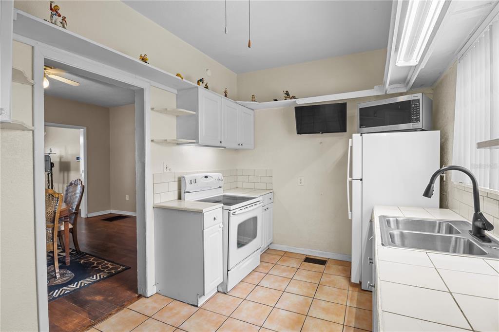 A kitchen with white cabinets, a white stove, a refrigerator, and tiled countertops and floors — 4517 KENILWORTH BOULEVARD, SEBRING, FL