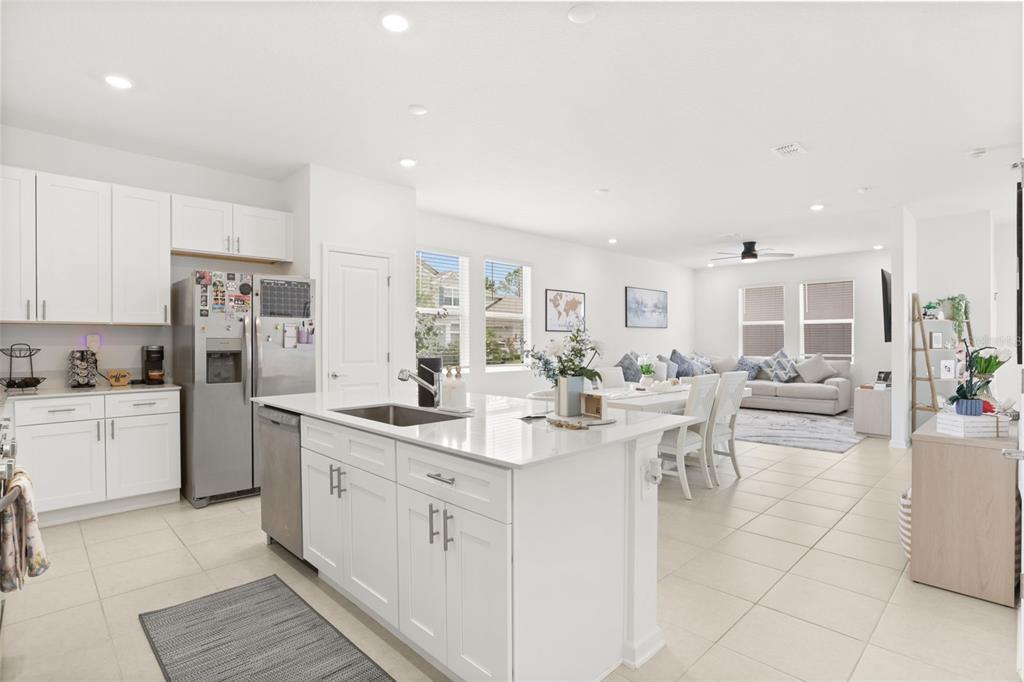 A bright, open-concept kitchen features white cabinetry, a central island, and a dining area beyond — 750 HONEYROCK STREET, DEBARY, FL