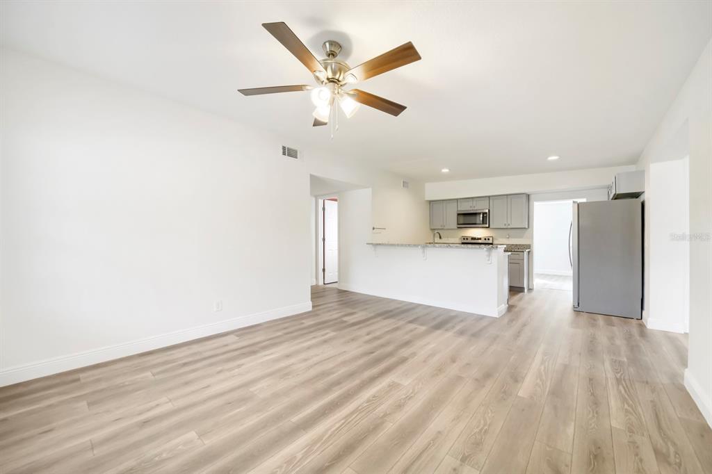 A living room with light wood-look flooring opens to a kitchen with gray cabinets — 201 HAYS DRIVE, SANFORD, FL