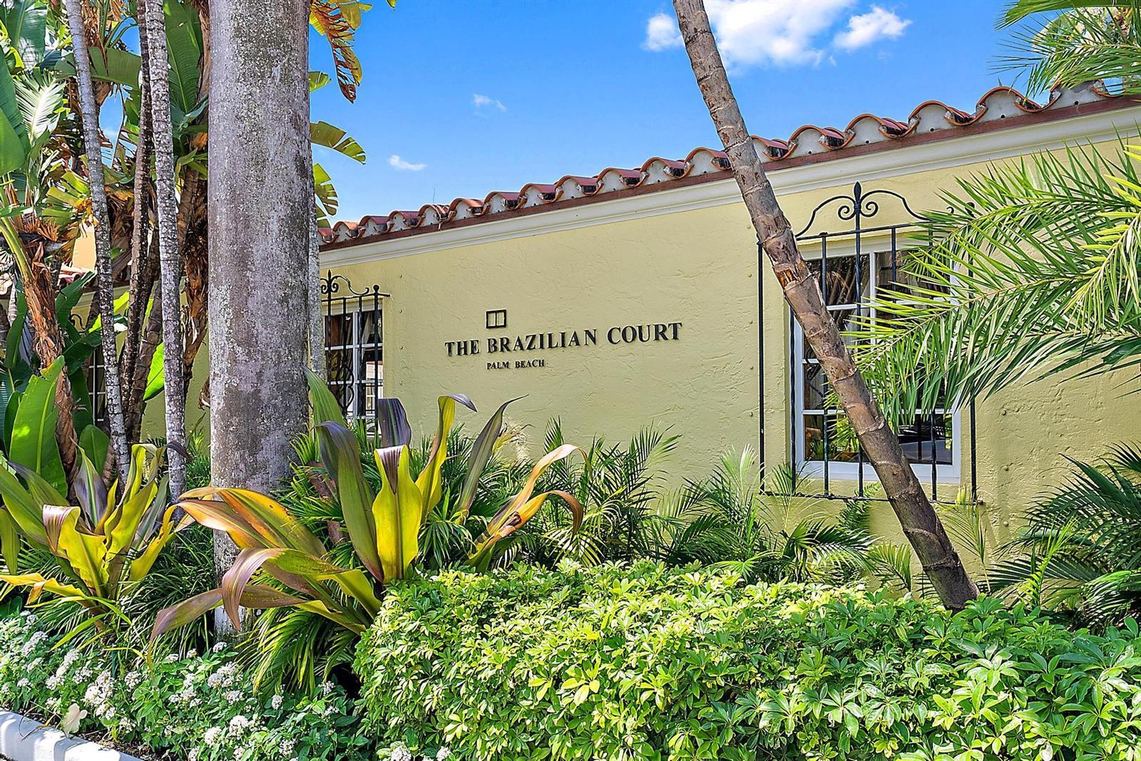The exterior of a yellow building features a sign reading The Brazilian Court Palm Beach — 301 Australian Avenue # 305, Palm Beach FL 33480, PALM BEACH, FL