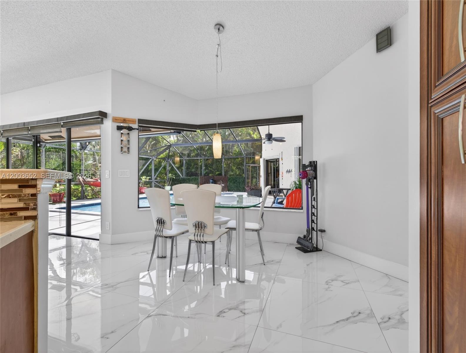 A dining area features a glass table, white chairs, marble-look tile floors, and pool views — 1025 Creekford Dr, Weston FL 33326, WESTON, FL