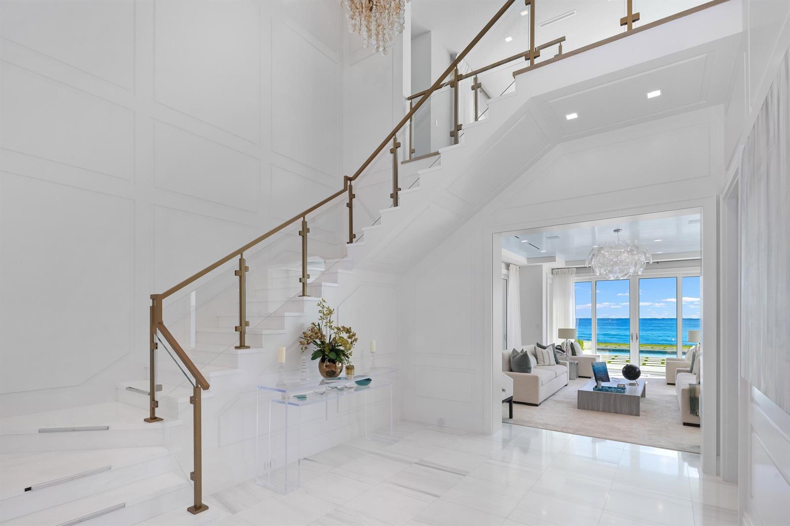 A bright foyer features a white staircase with a metal railing and ocean views beyond — 900 S Ocean Boulevard, Manalapan FL 33462, MANALAPAN, FL