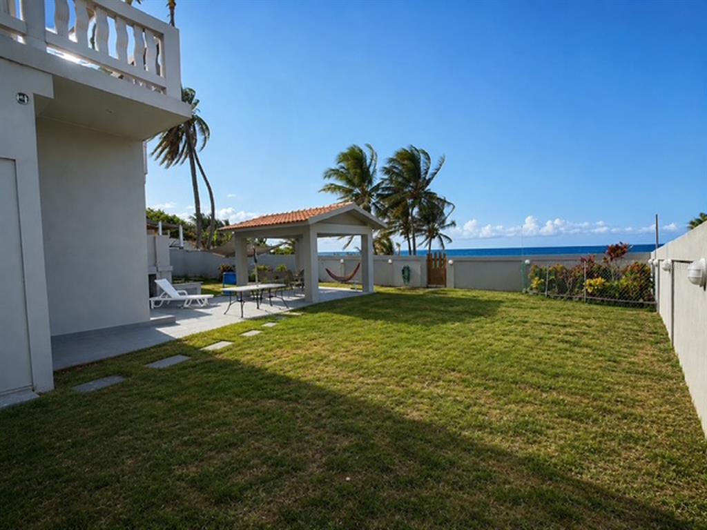 A grassy backyard features a covered patio area and a view of the ocean — Mameyal EXT KENNEDY UNIT Mameyal wd, DORADO, PR