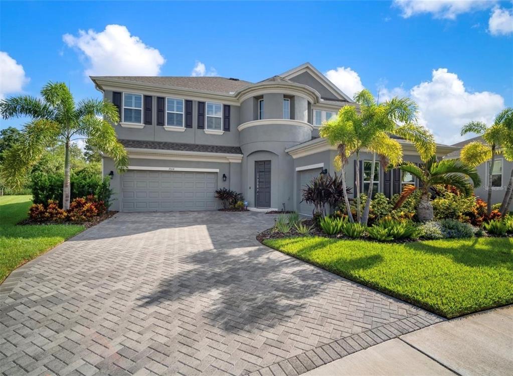 A two-story gray house with a paver driveway, a three-car garage, and palm trees — 7004 MAINLAND AVENUE, APOLLO BEACH, FL