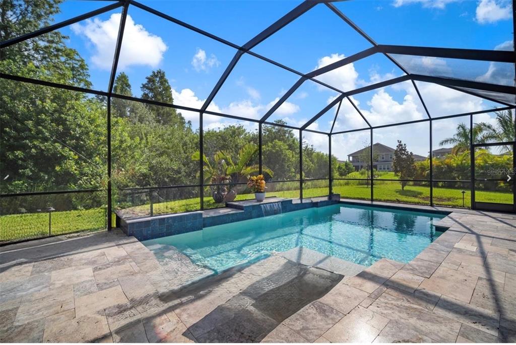 A swimming pool with a waterfall feature is enclosed by a screened lanai with stone pavers — 7004 MAINLAND AVENUE, APOLLO BEACH, FL
