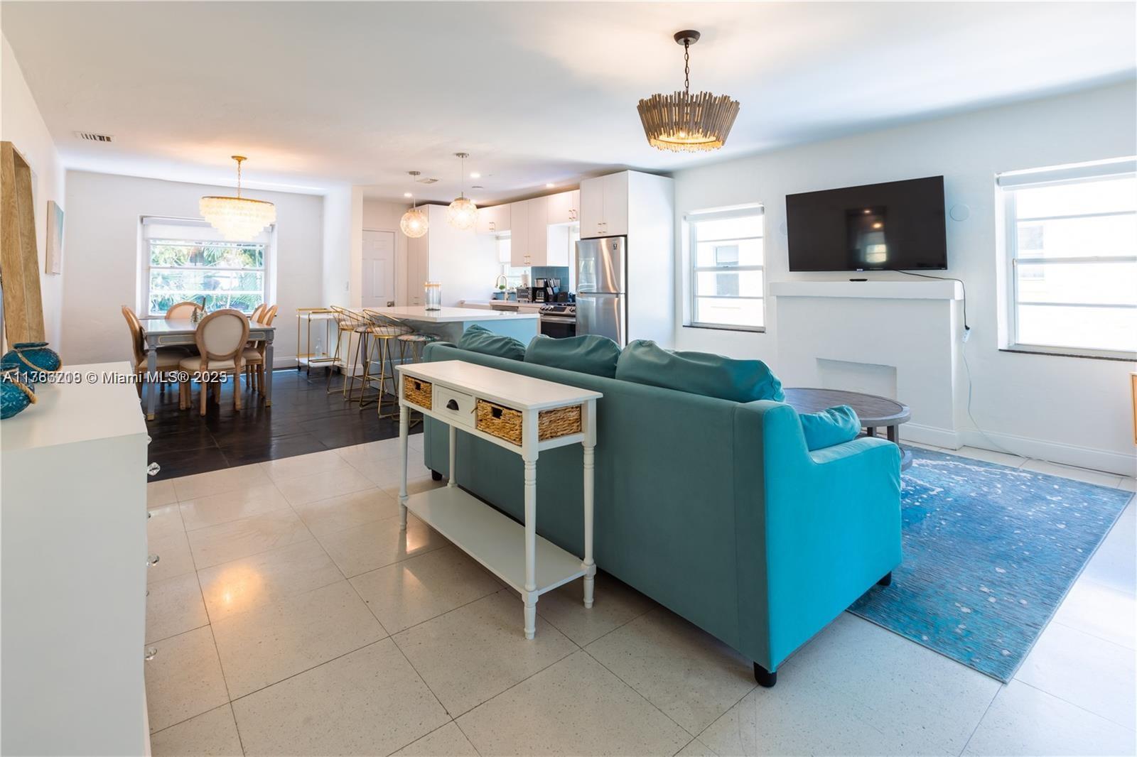 An open-concept living and dining area features a teal sofa, white cabinetry, and tile flooring — 426 NE 26th St, Miami FL 33137, MIAMI, FL
