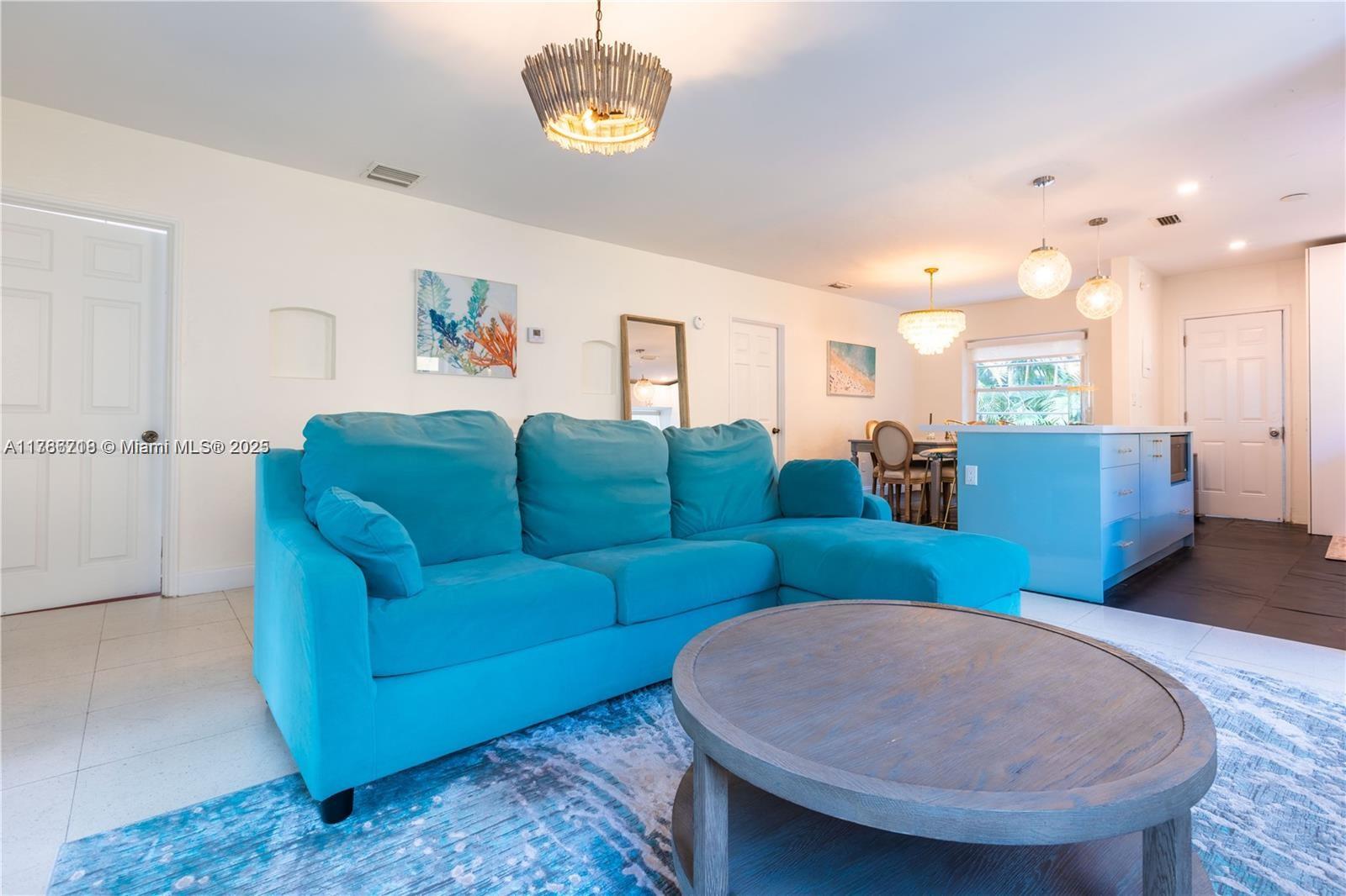 A living room features a bright blue sectional sofa, a round wooden coffee table, and pendant lighting — 426 NE 26th St, Miami FL 33137, MIAMI, FL