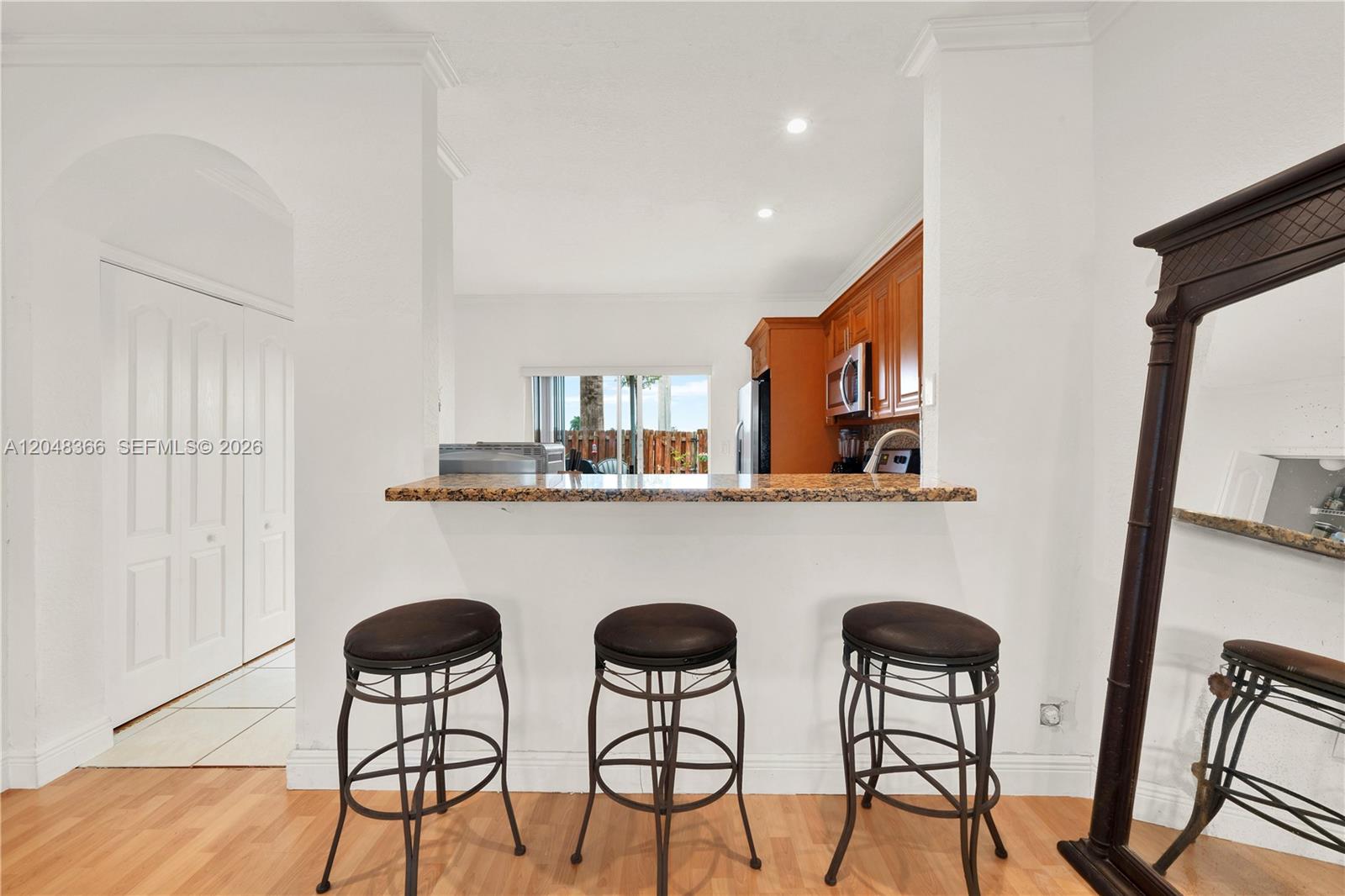 A kitchen pass-through features a granite breakfast bar with three stools and wood cabinets — 17066 SW 138th Ct # 17066, Miami FL 33177, MIAMI, FL
