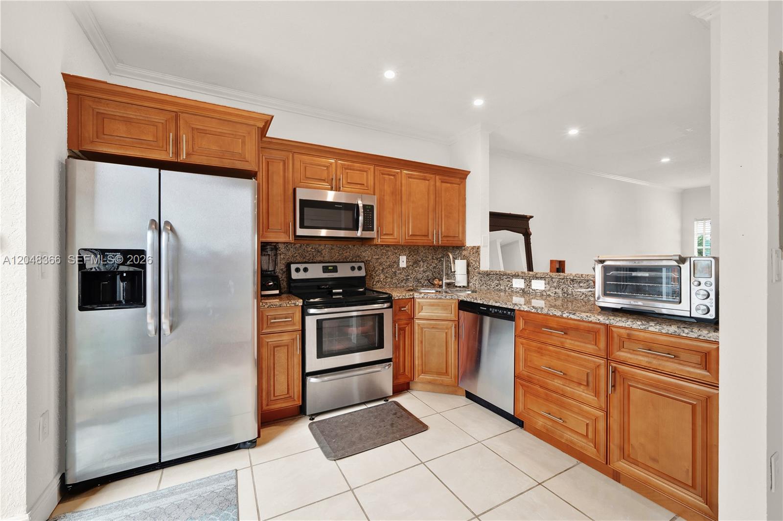 A kitchen features stainless steel appliances, wood cabinetry, and granite countertops over tiled flooring — 17066 SW 138th Ct # 17066, Miami FL 33177, MIAMI, FL