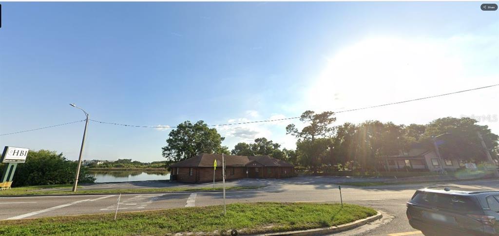 A low-rise commercial building sits near a pond beside a road under a bright sky — HWY 60 E, LAKE WALES, FL