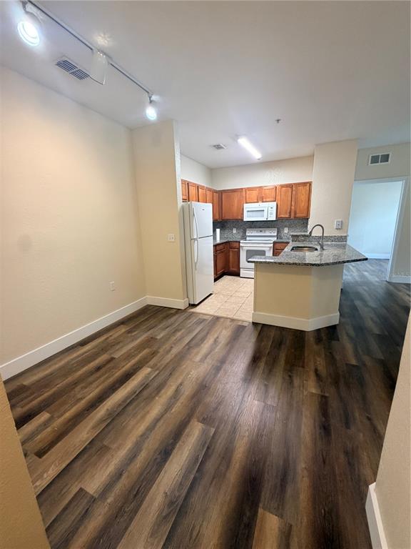 A kitchen with wood-look flooring, white appliances, granite countertops, and wood cabinetry — 8137 CLAIRE ANN DRIVE UNIT 207, ORLANDO, FL