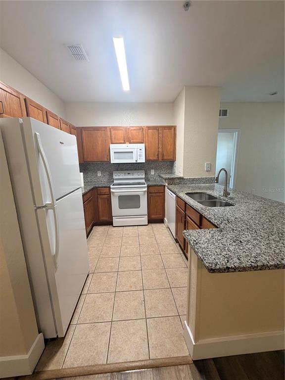 A kitchen features wood cabinets, granite countertops, white appliances, and light-colored tile flooring — 8137 CLAIRE ANN DRIVE UNIT 207, ORLANDO, FL