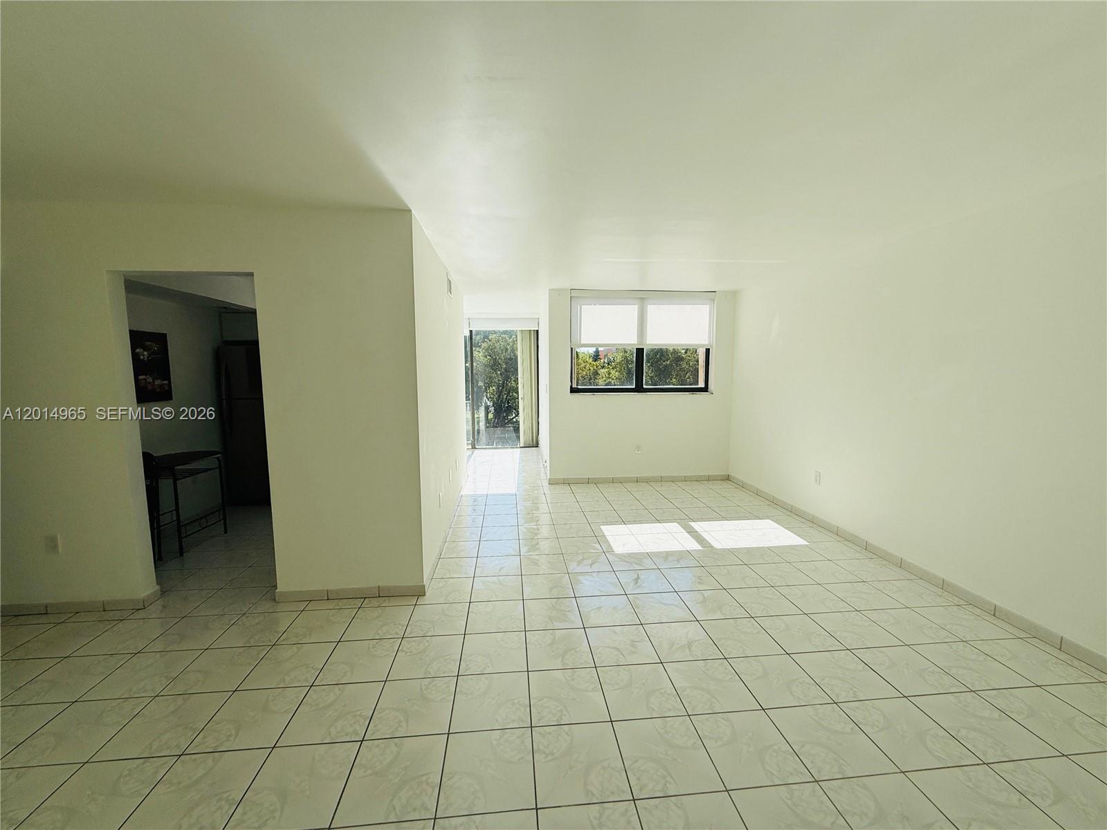 A bright, empty living area features white tiled floors, a large window, and a balcony — 9440 W Flagler St # 305, Miami FL 33174, MIAMI, FL