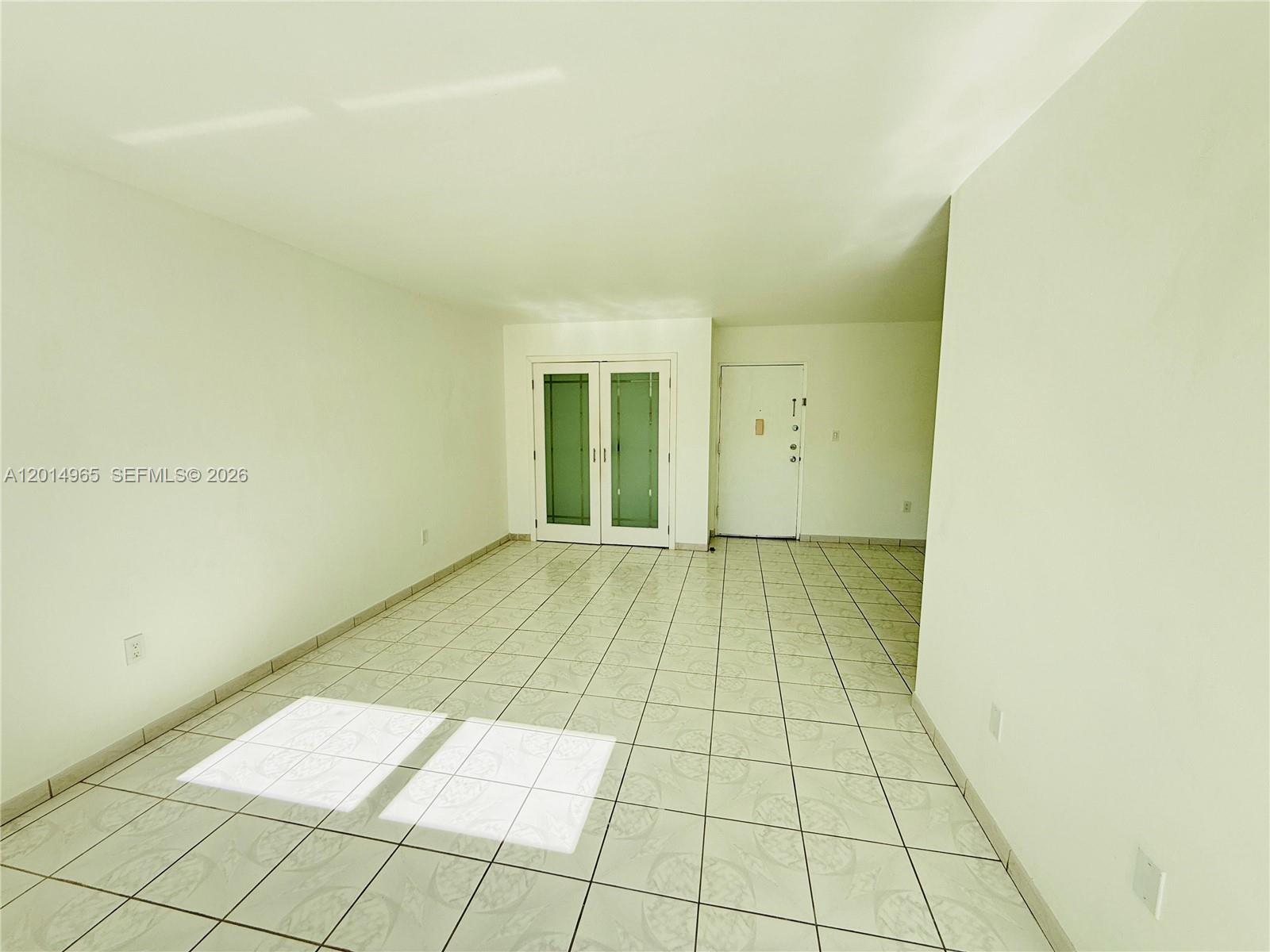 An empty room features white walls, light-colored tiled flooring, a white entry door, and French doors — 9440 W Flagler St # 305, Miami FL 33174, MIAMI, FL