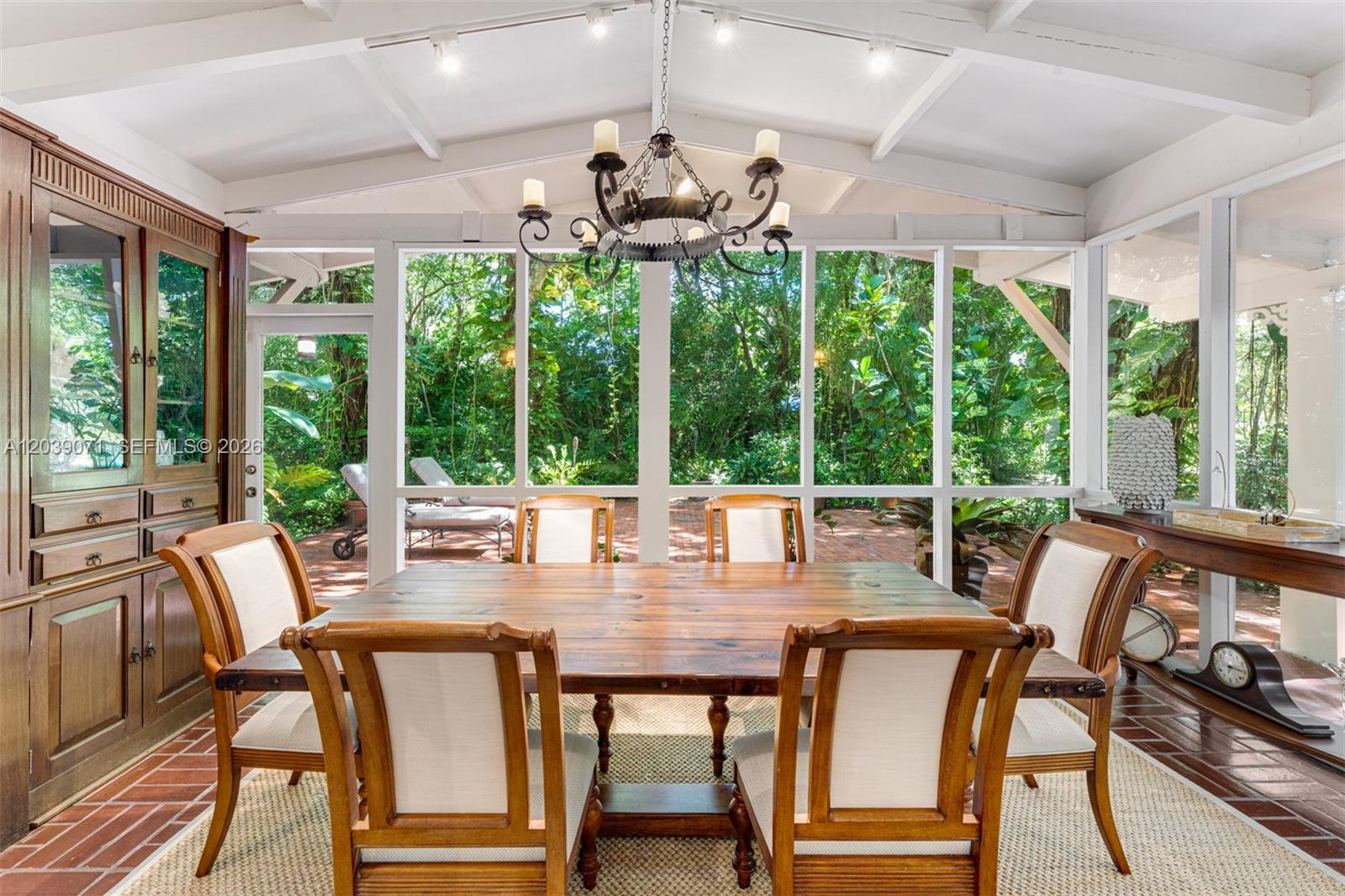 A dining room with a wooden table, chairs, and a chandelier overlooks a lush garden — 5950 SW 128th St, Pinecrest FL 33156, PINECREST, FL