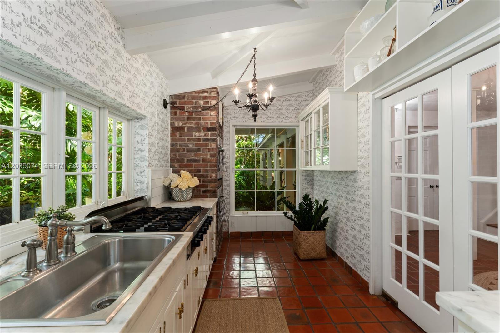 A kitchen with terracotta tile floors, a brick accent wall, and white cabinetry — 5950 SW 128th St, Pinecrest FL 33156, PINECREST, FL