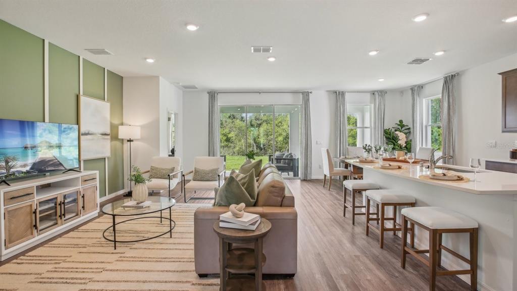 An open-concept living and dining area features a green accent wall, wood flooring, and island — 32745 WEATHERED OAK DRIVE, WESLEY CHAPEL, FL
