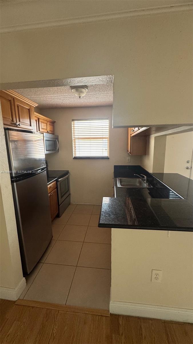 A galley-style kitchen features dark granite countertops, wood cabinetry, and stainless steel appliances — 2441 SW 31st Ave # 303, Miami FL 33145, MIAMI, FL