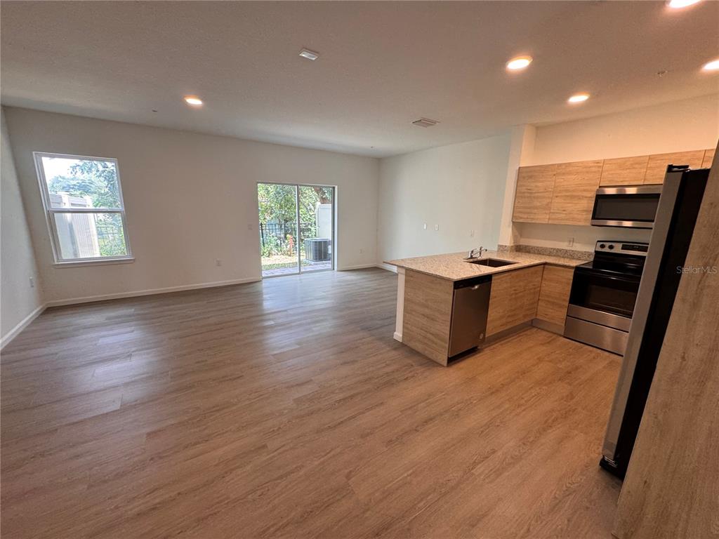 An open-concept kitchen and living area featuring light wood-look flooring and stainless steel appliances — 1209 SOUTHSTATION PLACE UNIT 308, ORLANDO, FL