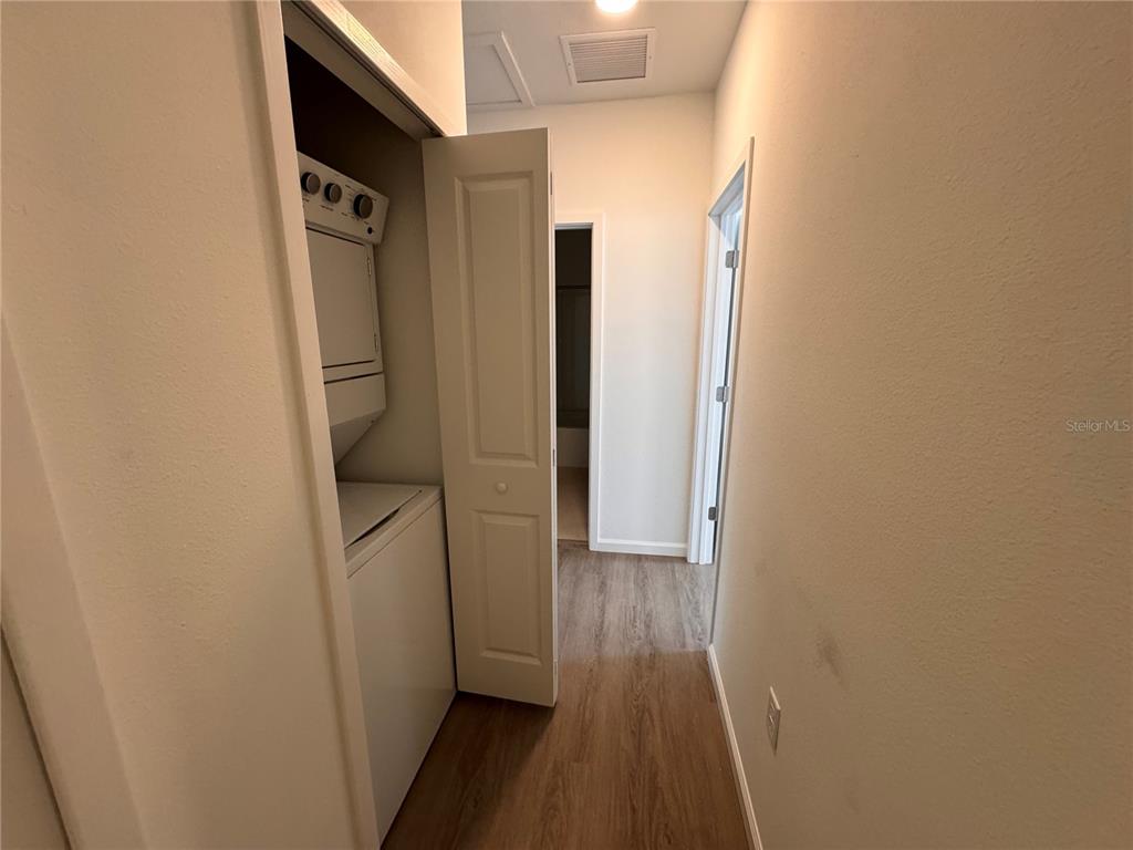 A laundry closet with a stacked washer and dryer sits in a hallway with wood-look flooring — 1209 SOUTHSTATION PLACE UNIT 308, ORLANDO, FL