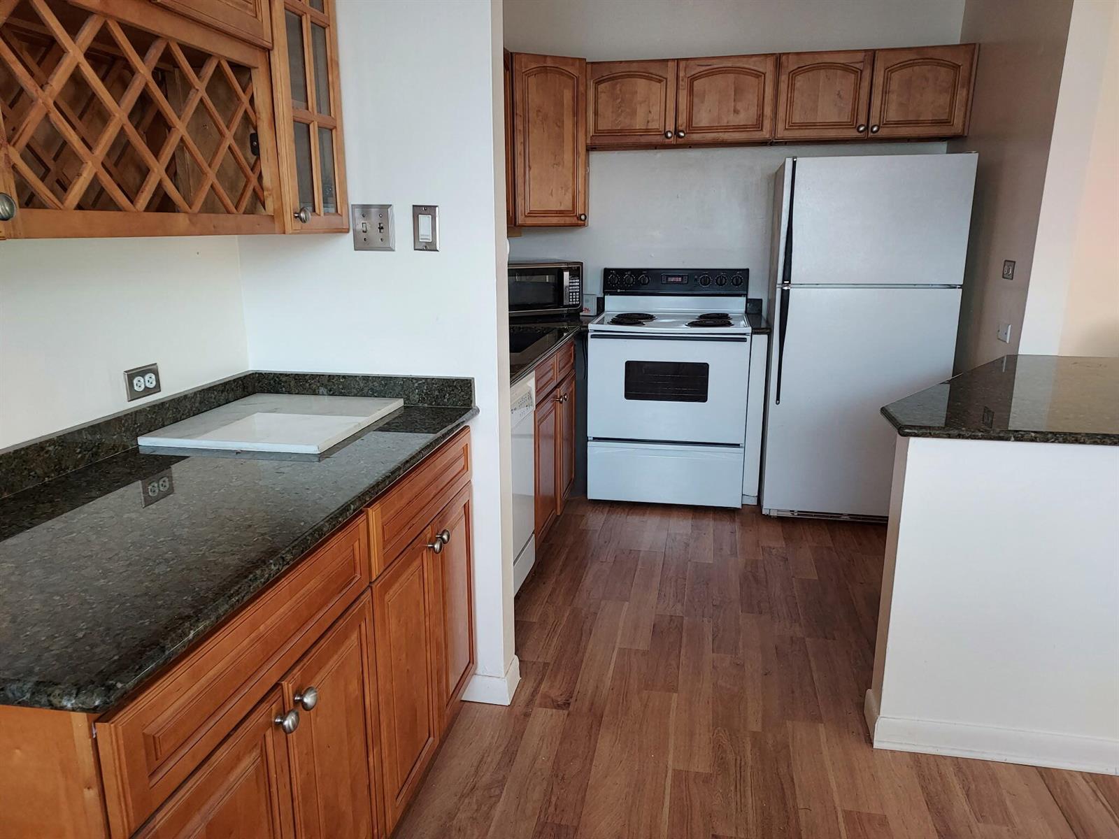 A kitchen features wood cabinets, dark granite countertops, white appliances, and wood-look flooring — 261 Coventry K, West Palm Beach FL 33417, WEST PALM BEACH, FL