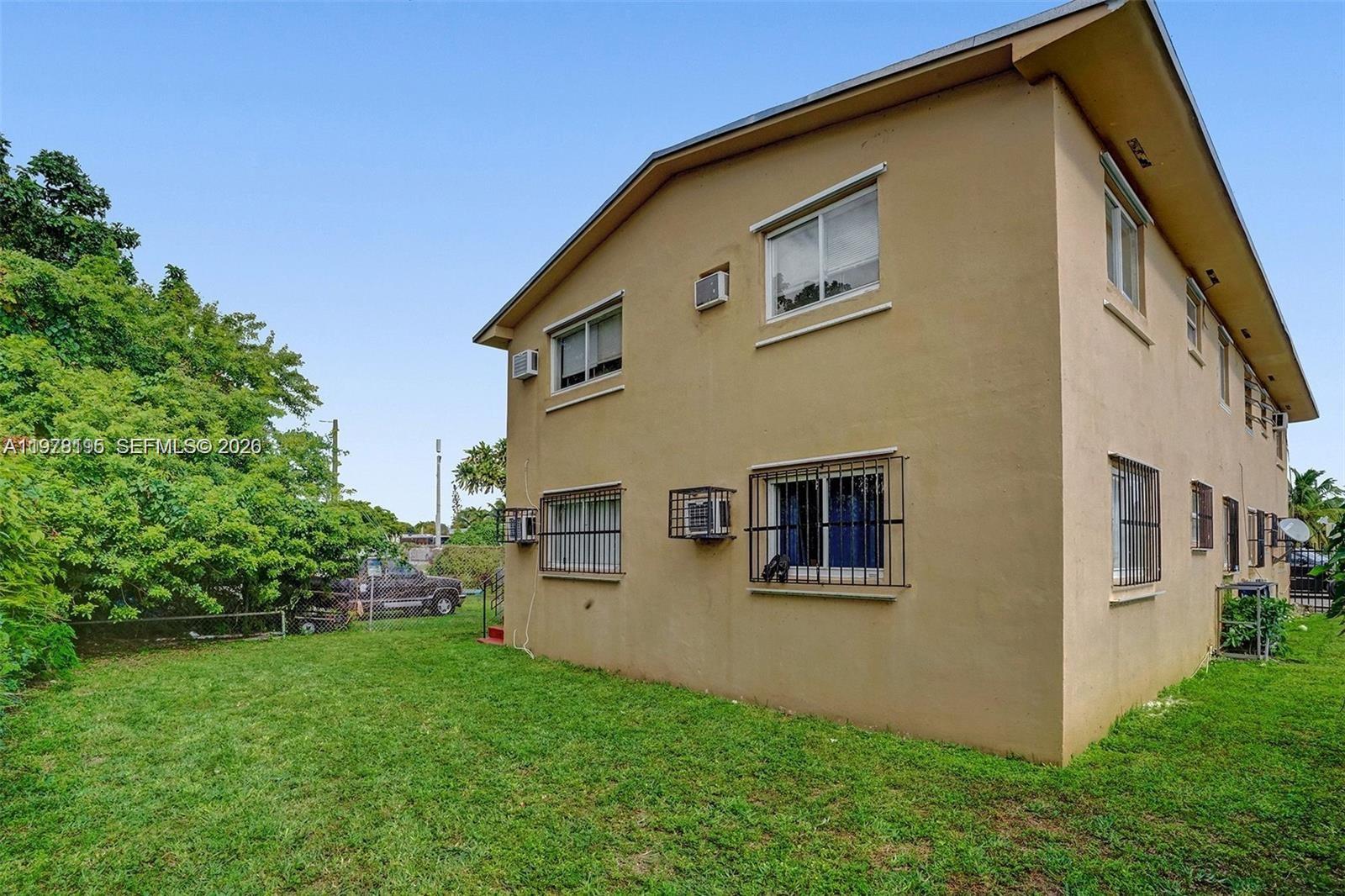 The exterior of a two-story tan building features multiple windows with security bars and air conditioners — 5842 NW 12th Ave, Miami FL 33127, MIAMI, FL