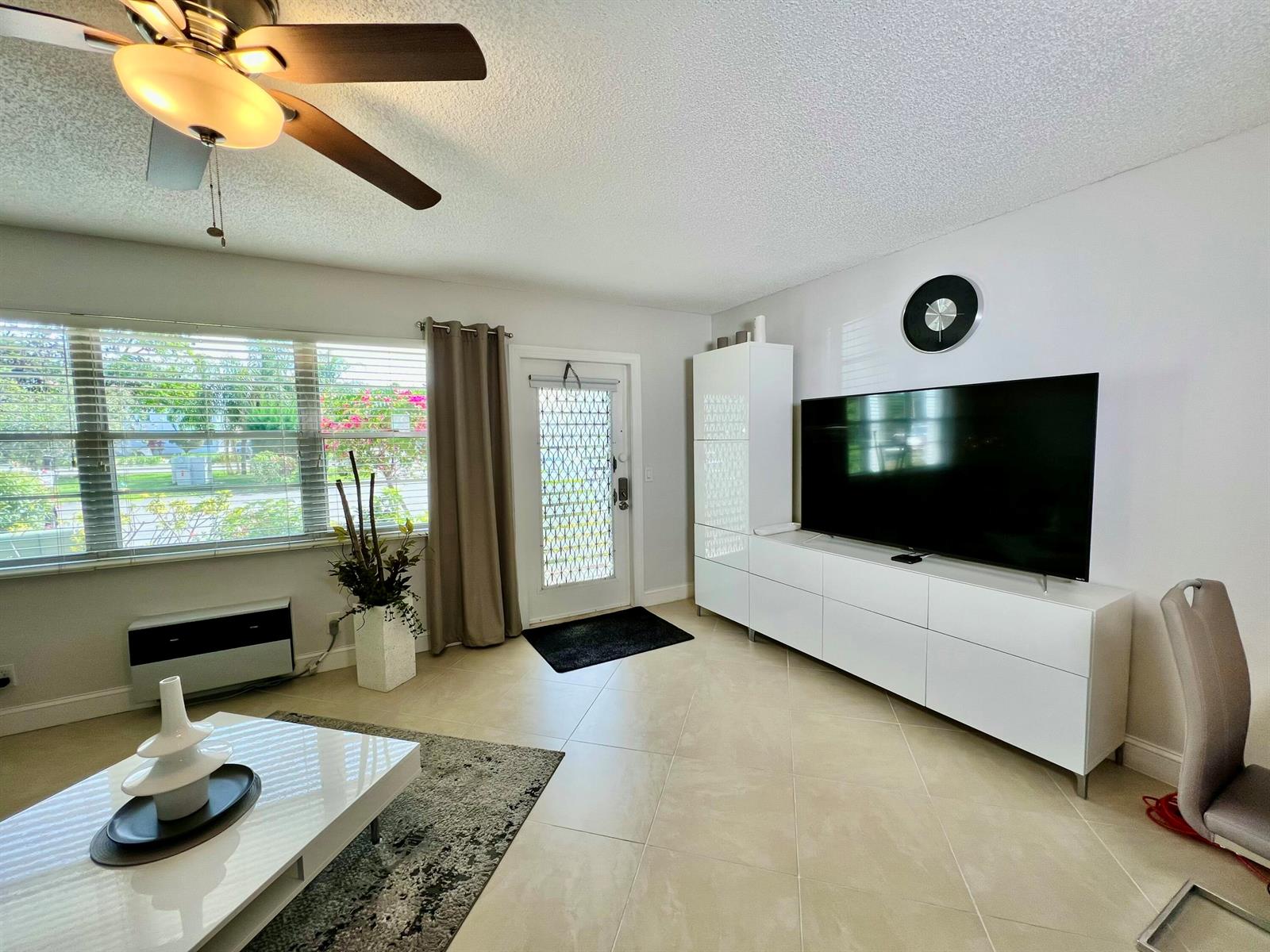 A living room features a ceiling fan, tiled floors, a large television, and a front door — 172 Tilford I, Deerfield Beach FL 33442, DEERFIELD BEACH, FL