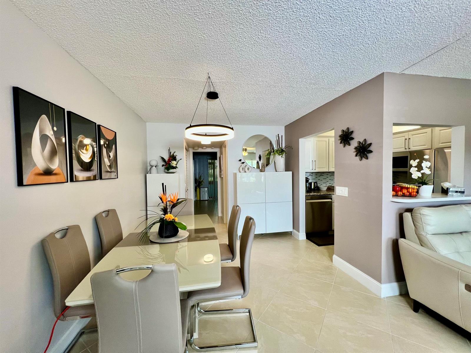 A dining area with a glass table, modern chairs, and a pendant light near a kitchen — 172 Tilford I, Deerfield Beach FL 33442, DEERFIELD BEACH, FL