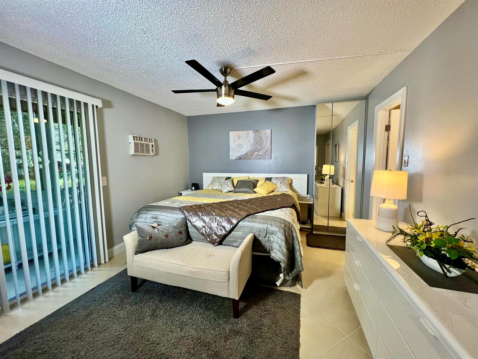 A bedroom features a bed with grey and yellow bedding, a ceiling fan, and mirrored closets — 172 Tilford I, Deerfield Beach FL 33442, DEERFIELD BEACH, FL
